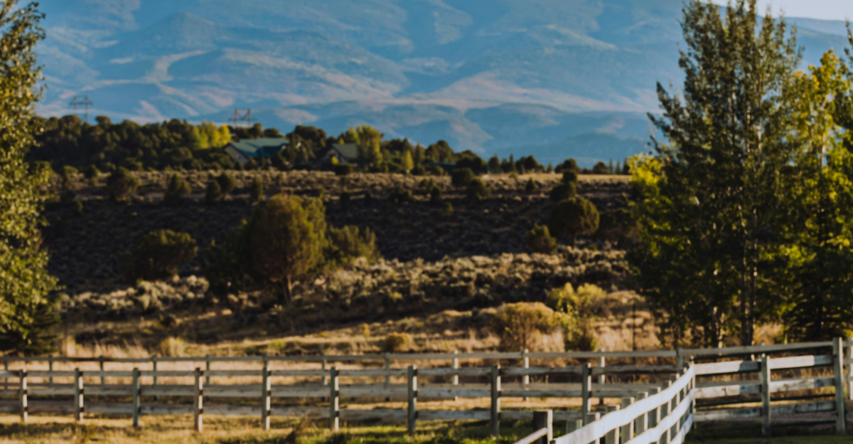 a wooden fence in a field with mountains in the background