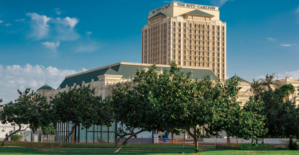 View of the Ritz-Carlton hotel in Jeddah surrounded by lush greenery and blue skies.