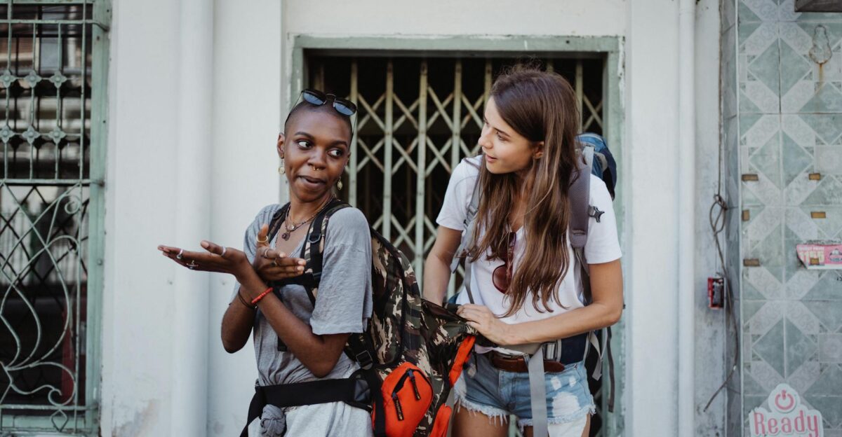 Two women stand laughing with backpacks exploring a city during their travel adventure
