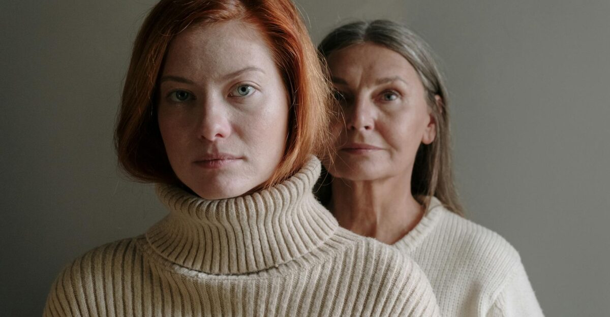 A serene portrait of a mother and daughter in cozy sweaters against a gray background