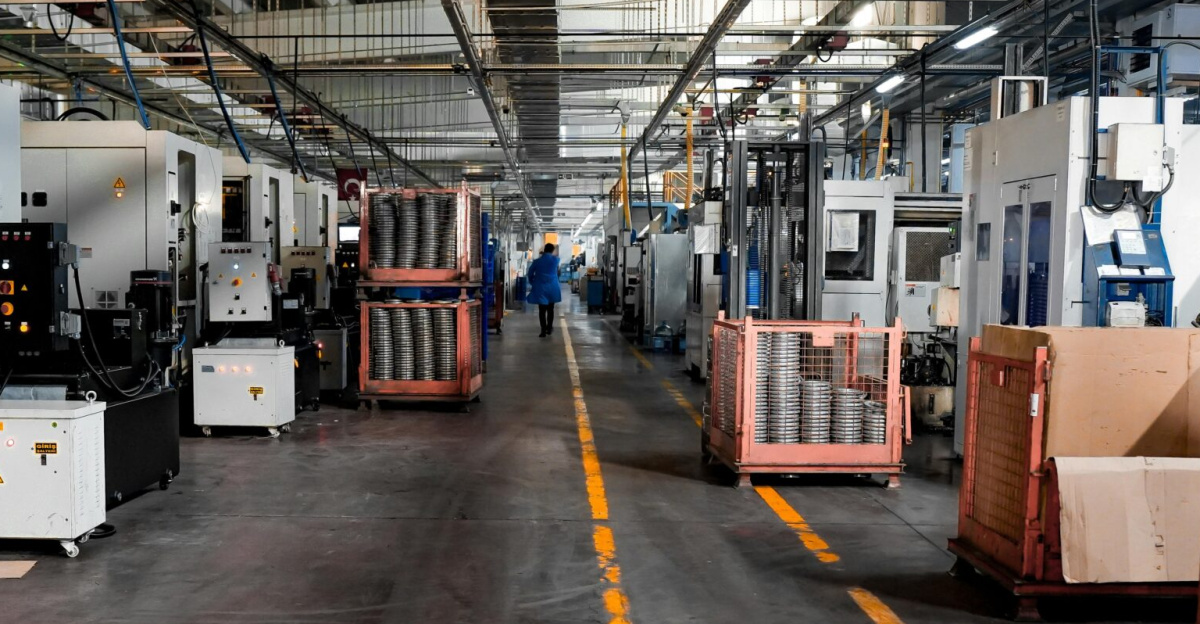 Vast industrial factory floor with machinery, crates, and structured workstations.