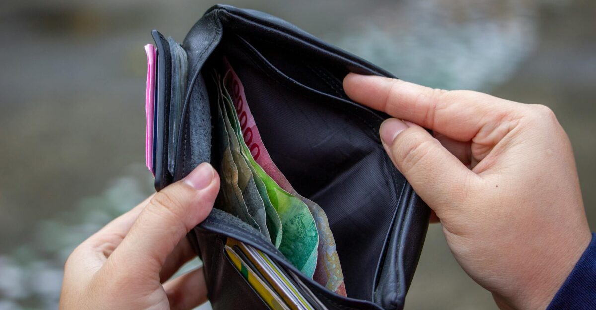 Person holding open wallet revealing banknotes including Indonesian rupiah in an outdoor setting