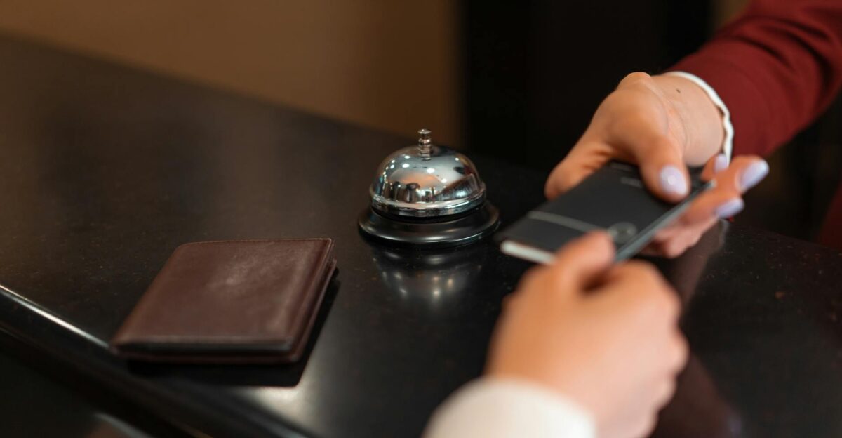 A close-up of a hotel check-in process with a smartphone and card transaction at the reception desk