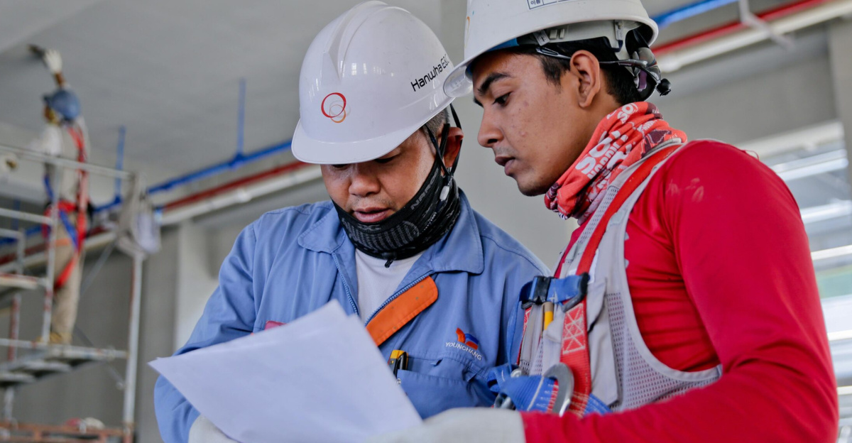 Two engineers in safety helmets reviewing construction plans at a worksite.