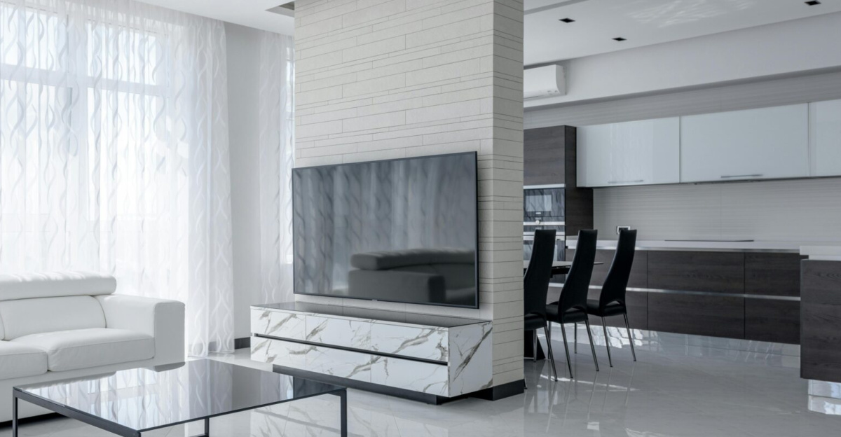 Interior of light apartment with table and couch near TV with cabinet and white walls near window with curtains and stool near lamp