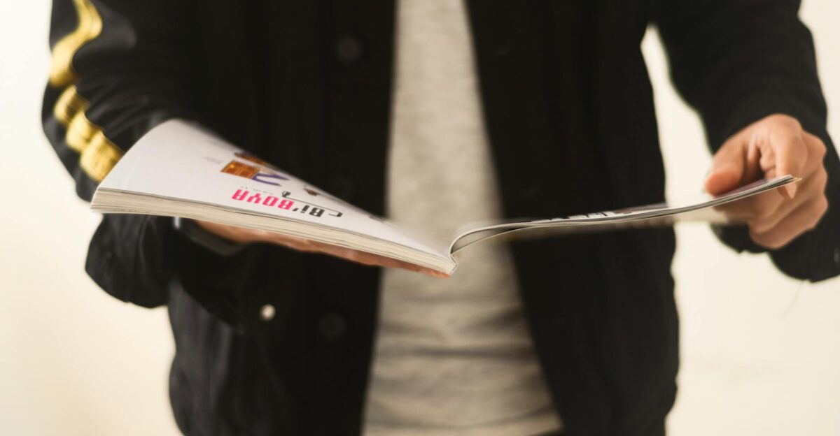 Close-up of a man in a casual jacket flipping through a magazine
