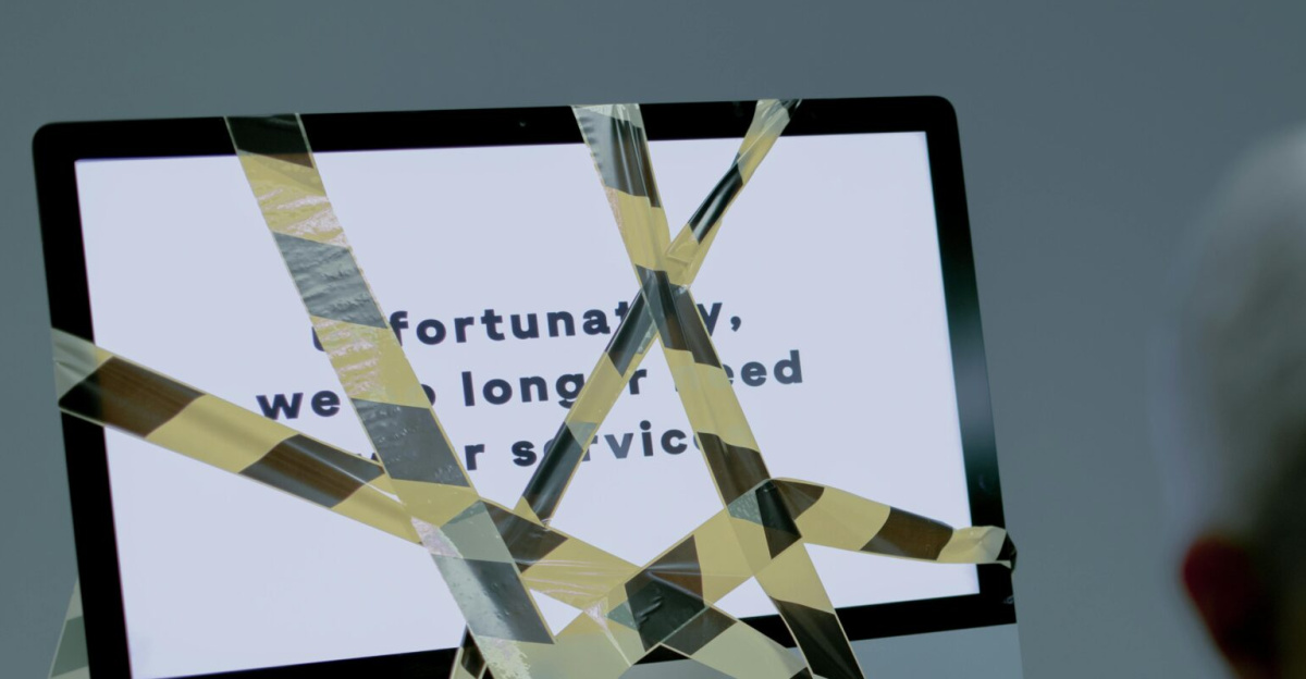 A senior man facing the reality of unemployment highlighted by a computer screen and warning tape.