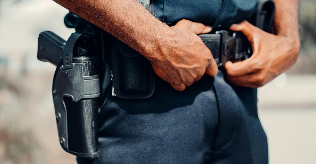 A police officer adjusts their utility belt outdoors showcasing law enforcement gear and uniform