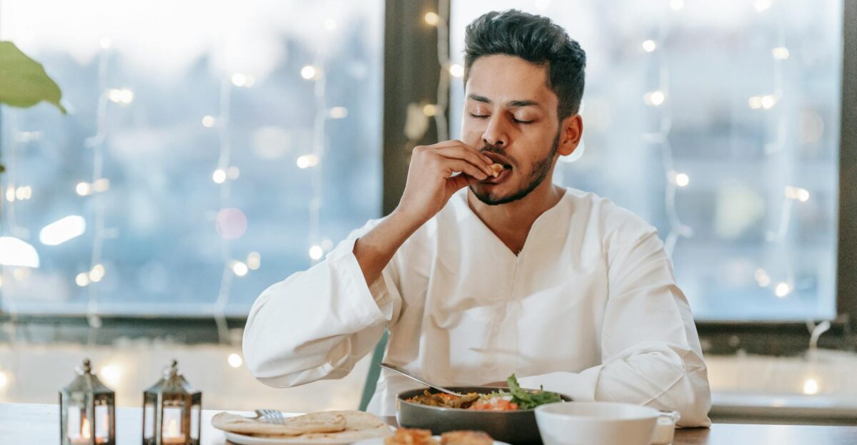 A man in a white thobe savoring a traditional meal indoors with string lights background