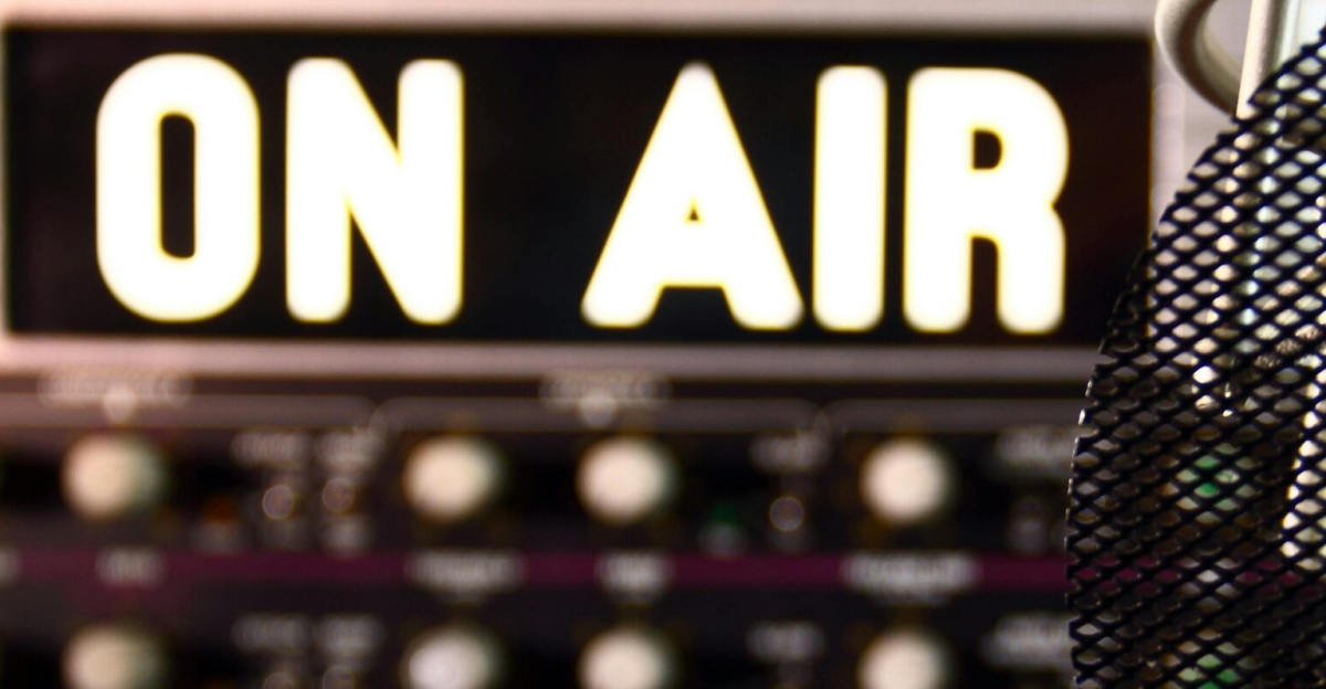 Close-up of a radio microphone and control panel in an illuminated studio.