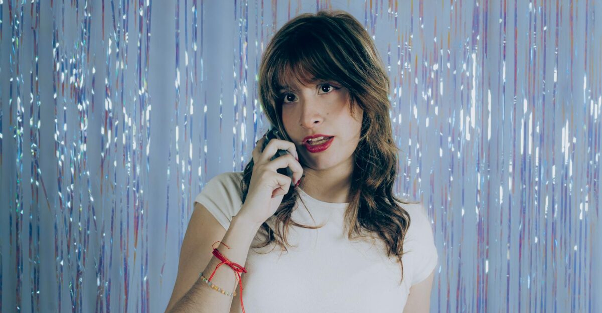 Portrait of a young woman with phone posing in front of sparkling blue backdrop